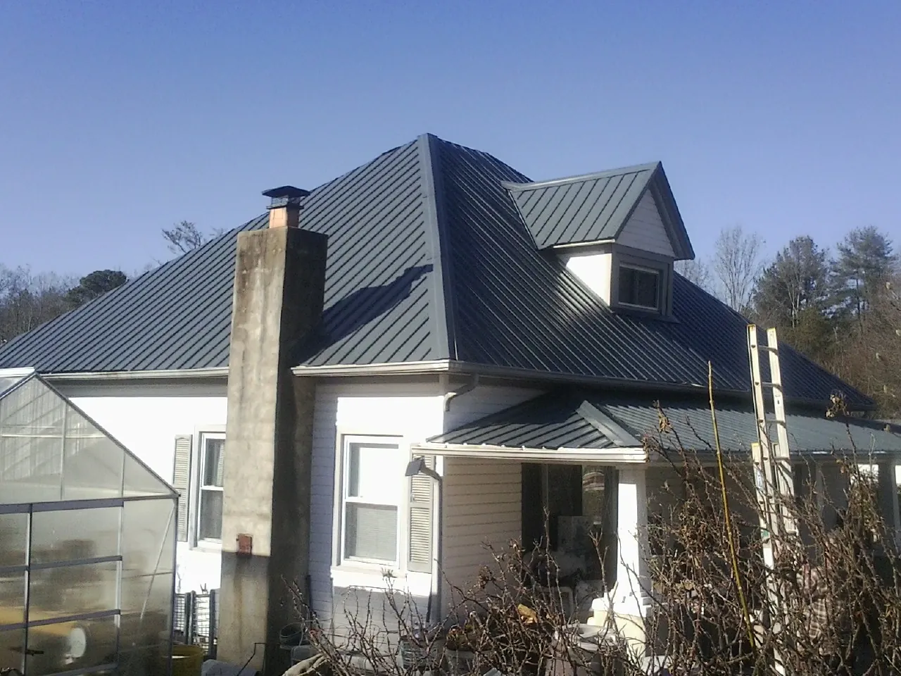 Dark blue standing seam metal roof on a white farmhouse with dormer — Slate & Tile Roof Repair by Roofing Brothers in Diggs