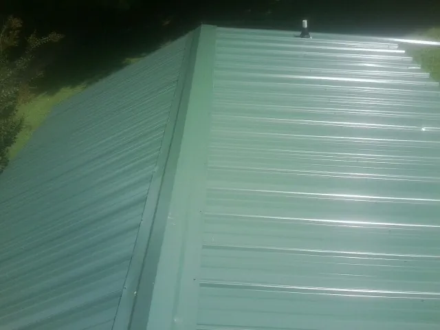 New green metal panels meeting at the ridge of a roof — Flat Roof Repair work by our crew in Diggs