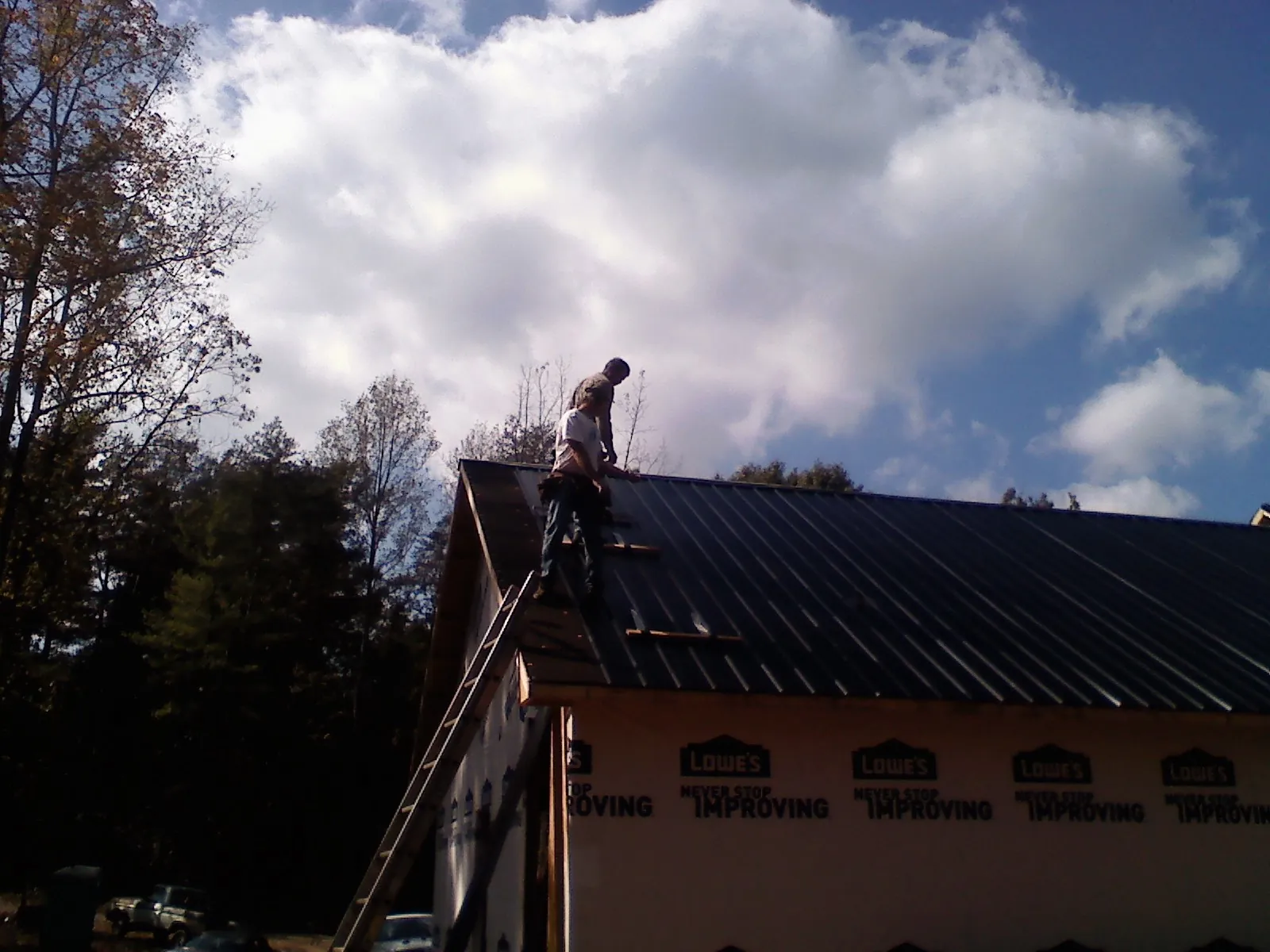 Roofer fastening dark metal panels high against a cloudy sky, from a Roof Inspection job in Diggs