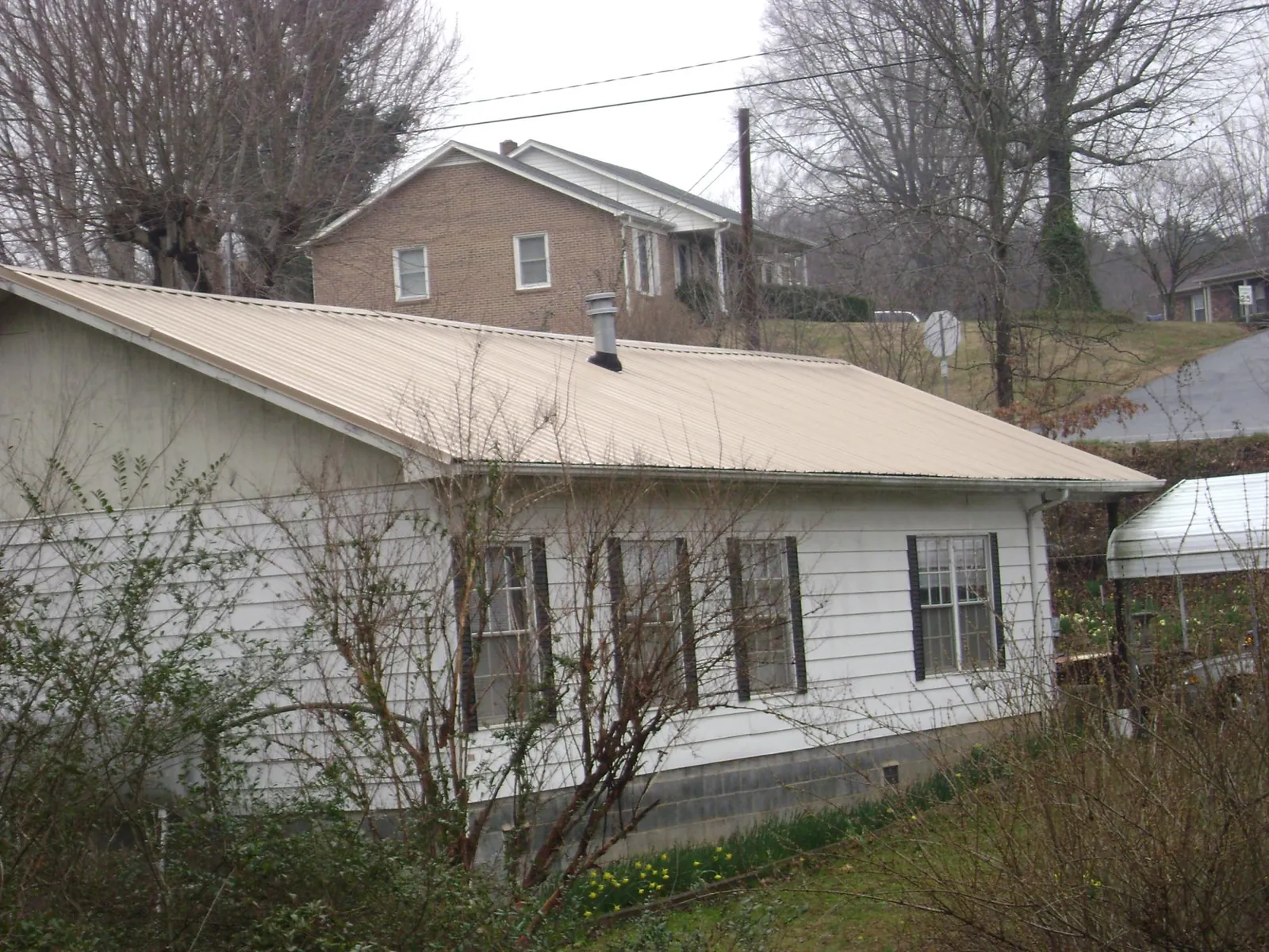 Tan metal roof on a white sided house set into a hillside — Commercial Roofing by Roofing Brothers in Diggs